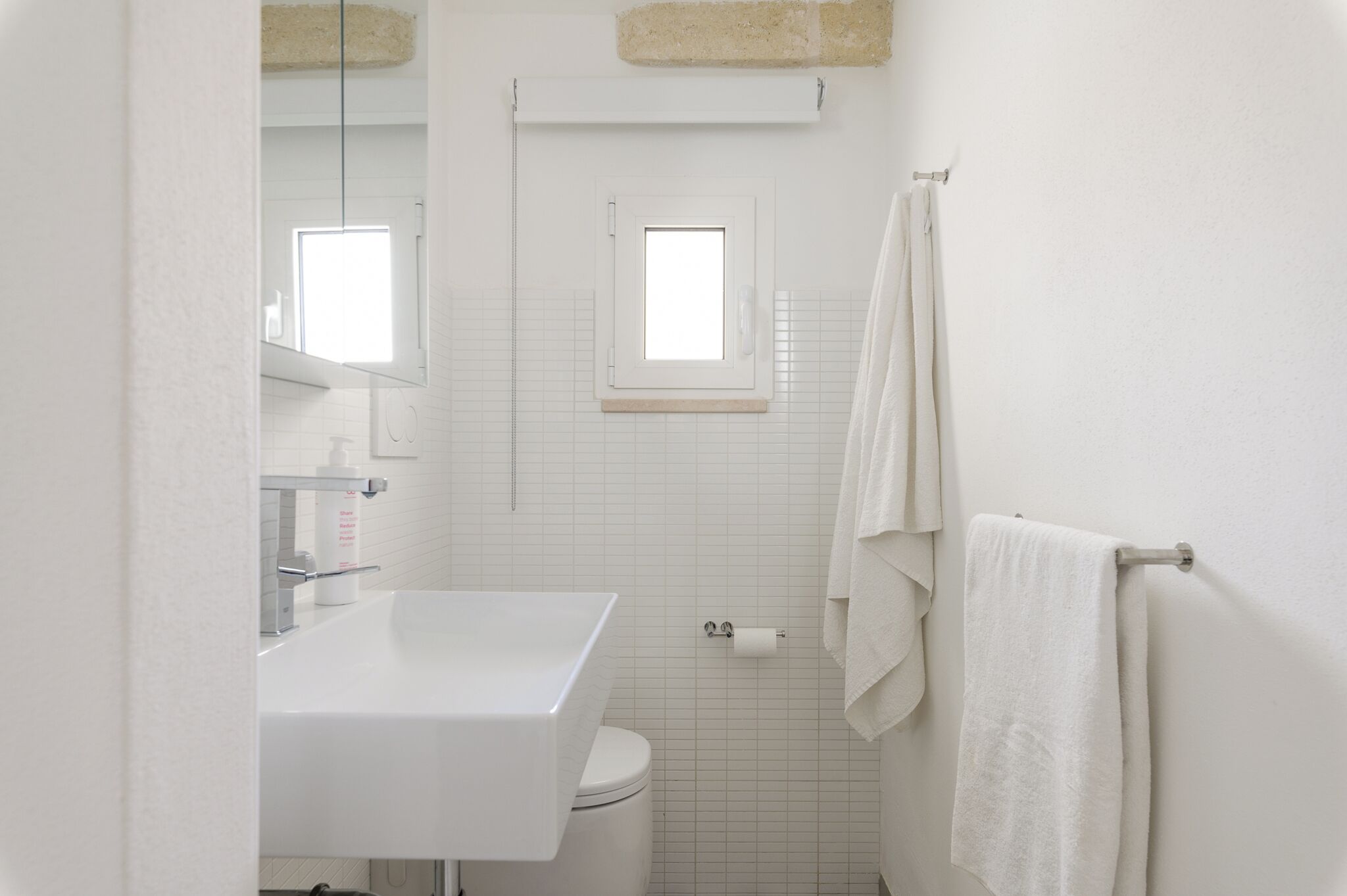 A bathroom with a white sink, toilet, and a window above the toilet.