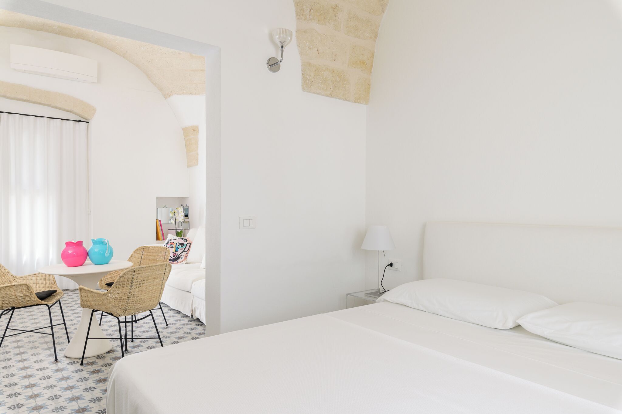 Een hotelkamer met een bed, een kleintje tafeltje met stoelen, een lamp en een wandlamp.