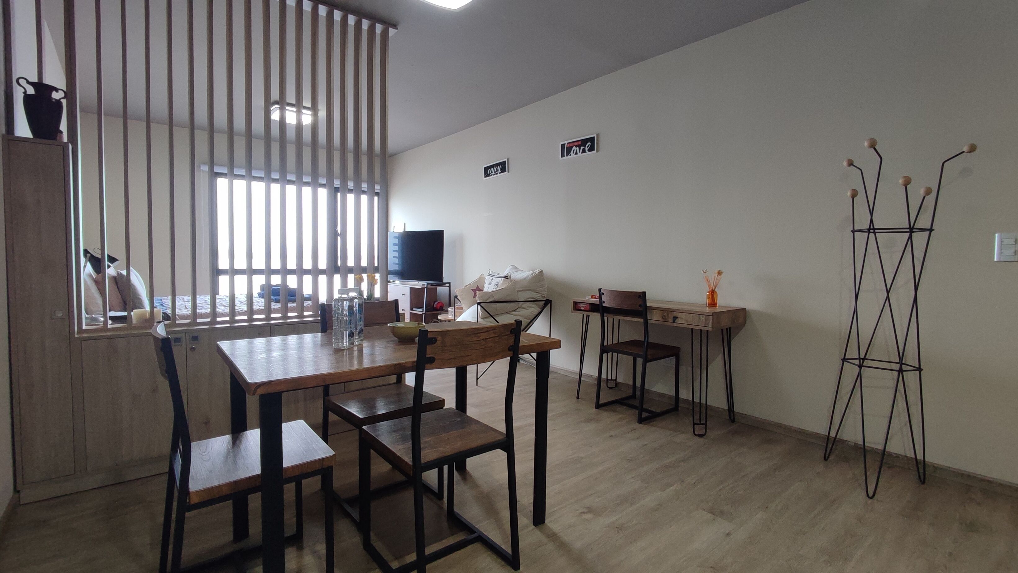 Quarto com mesa de jantar, cadeiras, televisão, escrivaninha e planta decorativa.