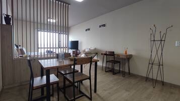 Quarto com mesa de jantar, cadeiras, televisão, escrivaninha e planta decorativa.