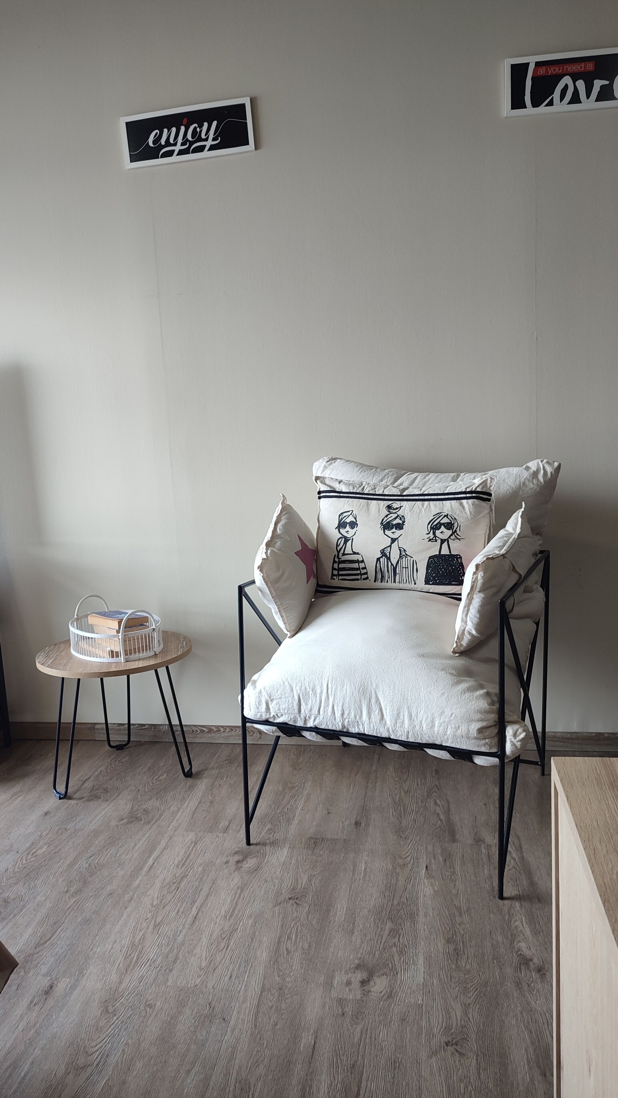 A minimalist room with a sofa, pillows, a small round table with a basket, and two wall signs.