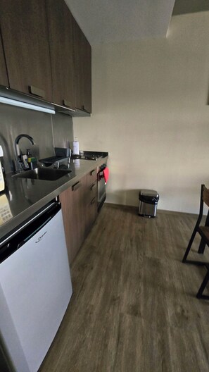 A compact kitchen with a dishwasher, a sink, and a small trash bin.