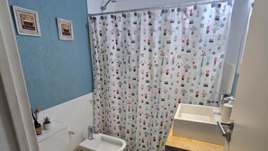 Un bagno con toilette, bidet, tenda da doccia con motivi floreali e lavandino.