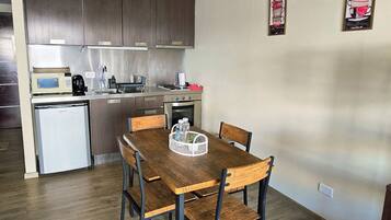 A compact kitchen with modern appliances, a dining area with a wooden table and chairs, and a small refrigerator.