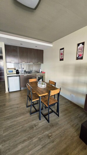 A compact kitchen with modern appliances, a dining area with a wooden table and chairs, and a small refrigerator.
