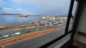 A view of a marina with boats, a parking lot, and a road with a pedestrian walkway. - Sunrise in front of the Beagle Channel, everything close by! (Ushuaia)