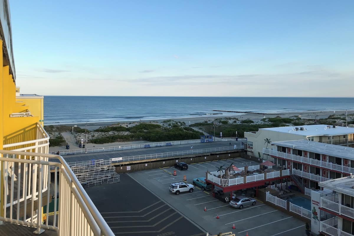 A view of a parking lot with a beach in the background, a building with a sign reading "Sahara Motel," and a clear sky.