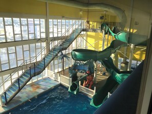 Un parque acuático interior con una piscina grande, varias toboganes y una escalera que lleva a niveles superiores.