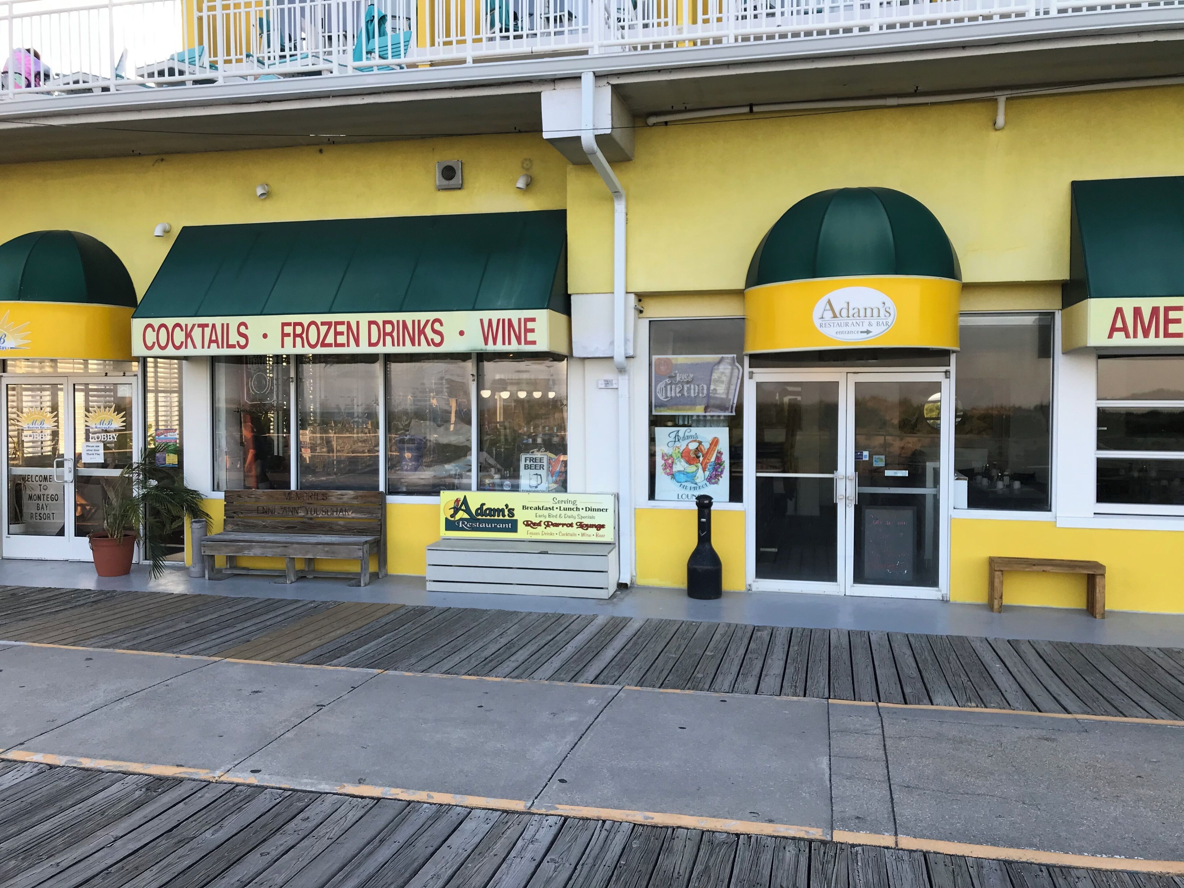 A waterfront restaurant with a yellow facade and green awnings, offering cocktails, frozen drinks, and wine.
