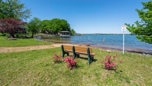 A bench by a lake with a warning sign, a gazebo, and a house in the background.