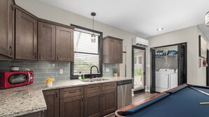 A kitchen with dark wooden cabinets, a red microwave, a sink, and a pool table.