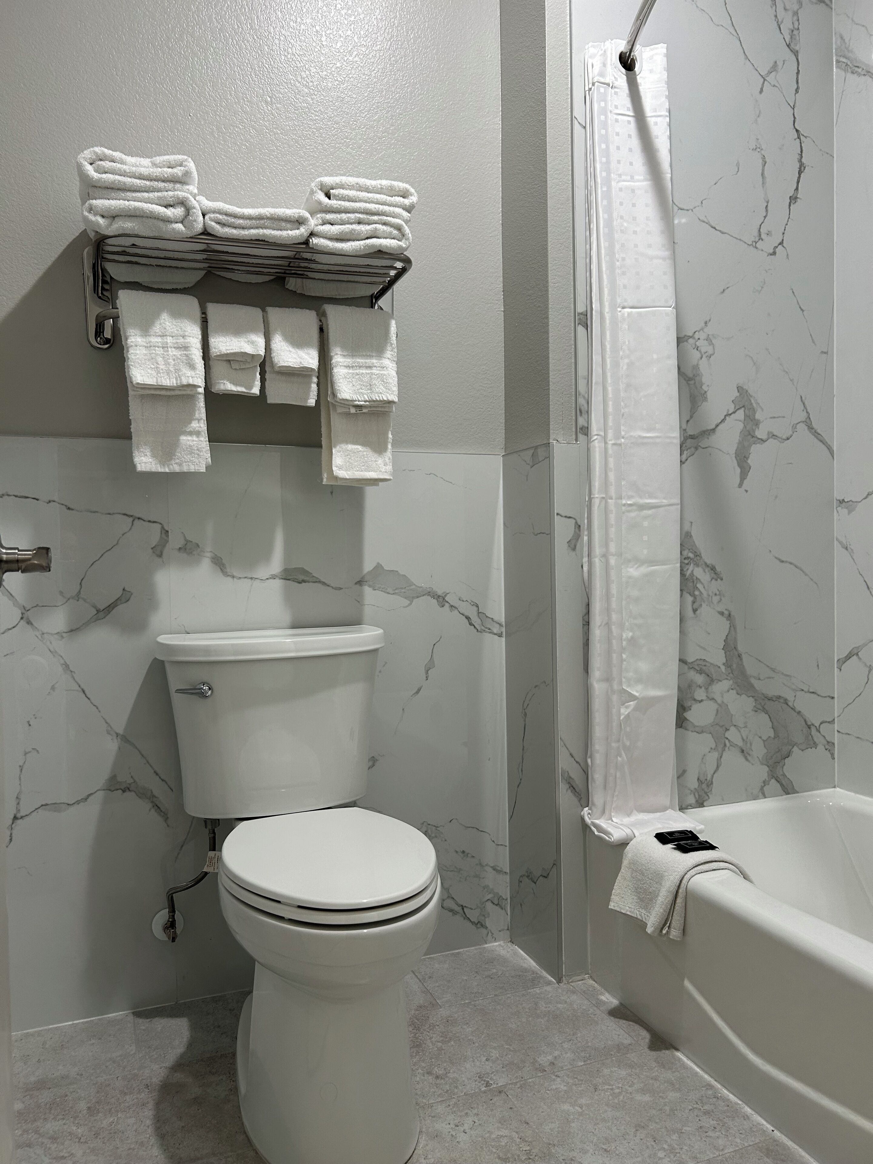 A bathroom with a toilet, a stack of towels, a shower curtain, and a bathtub.