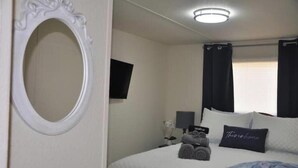 Una camera da letto con un letto, un comodino, una lampada, una TV a muro e una finestra con tende.