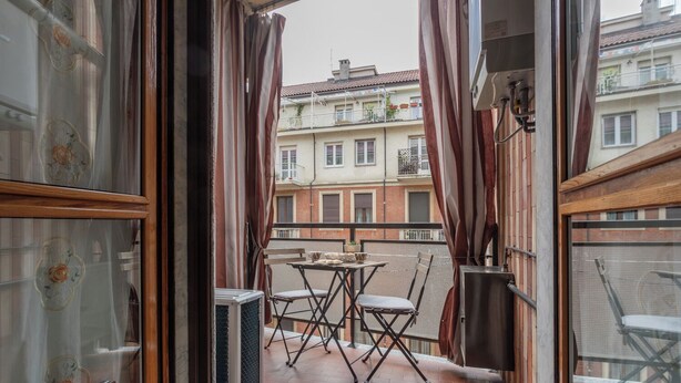 Een balkon met een tafel, stoelen, een bloempot en gebouwen op de achtergrond.