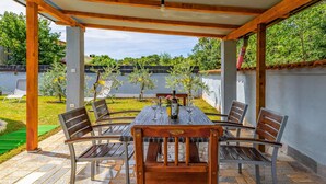 Un patio al aire libre cubierto con una mesa y sillas de madera, una botella de vino y un jarrón de flores.