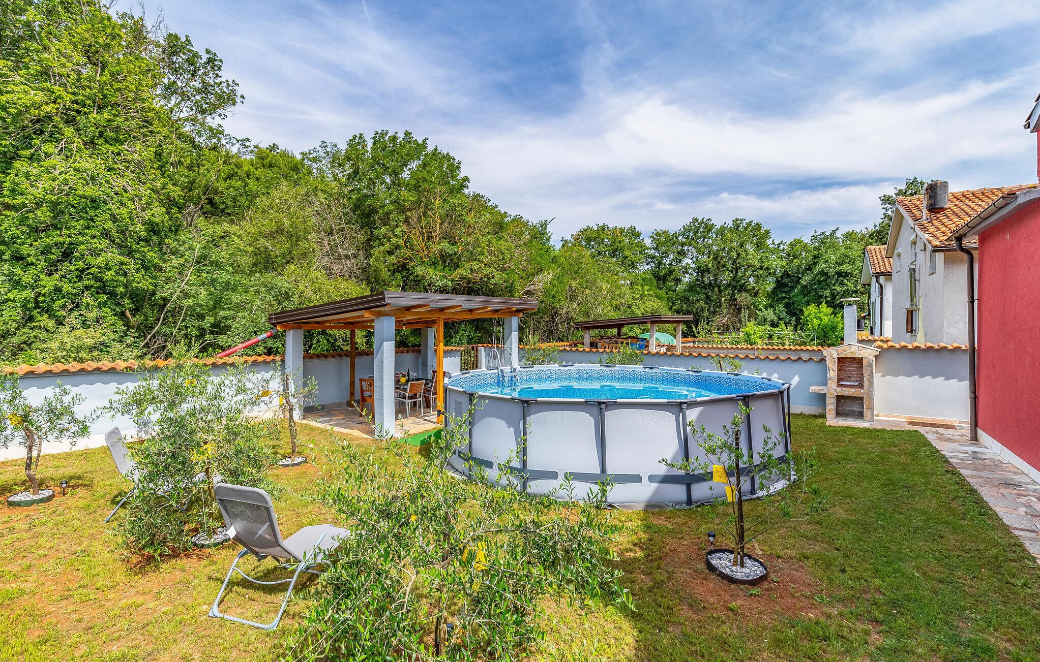 A backyard with a swimming pool, a covered patio, and a small garden area.