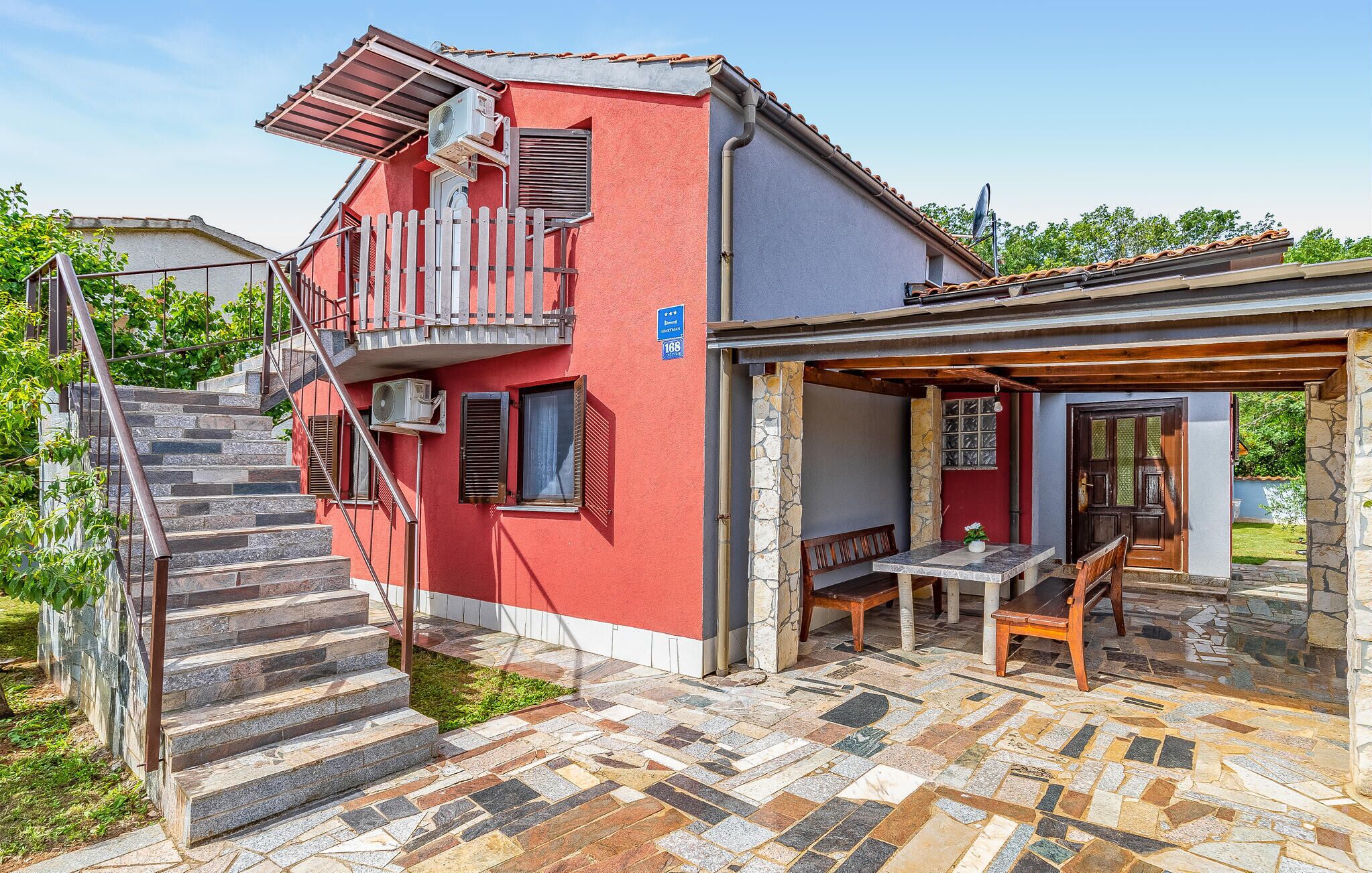 Een rood gebouw met een stenen trap die leidt naar een balkon, een overdekt terras en een stenen muur.