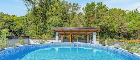 A swimming pool with a pergola structure, surrounded by lush greenery.