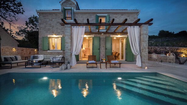Een stenen gebouw met een zwembad, groene luiken en terras.