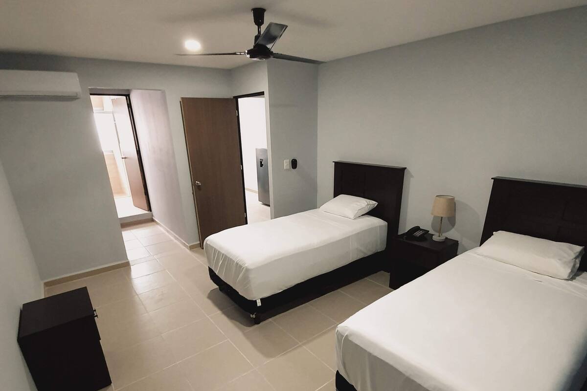 A hotel room with two beds, a ceiling fan, and a small bedside table with a lamp.