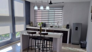 A modern kitchen with a central island, bar stools, pendant lights, and a built-in refrigerator. - Torre Metropoli (Cancun)