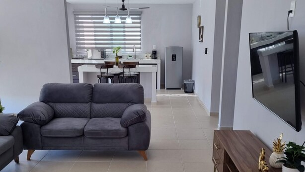 A modern living room with a grey sofa, a wooden TV stand, and a kitchen in the background. - Torre Metropoli (Cancun)
