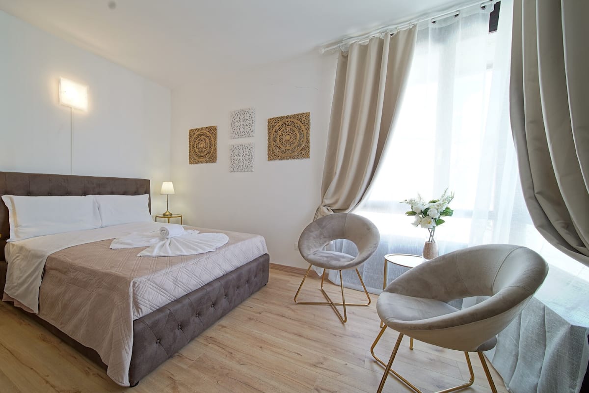 A hotel room with a bed, two bedside lamps, a chair, a small table, and decorative wall art.
