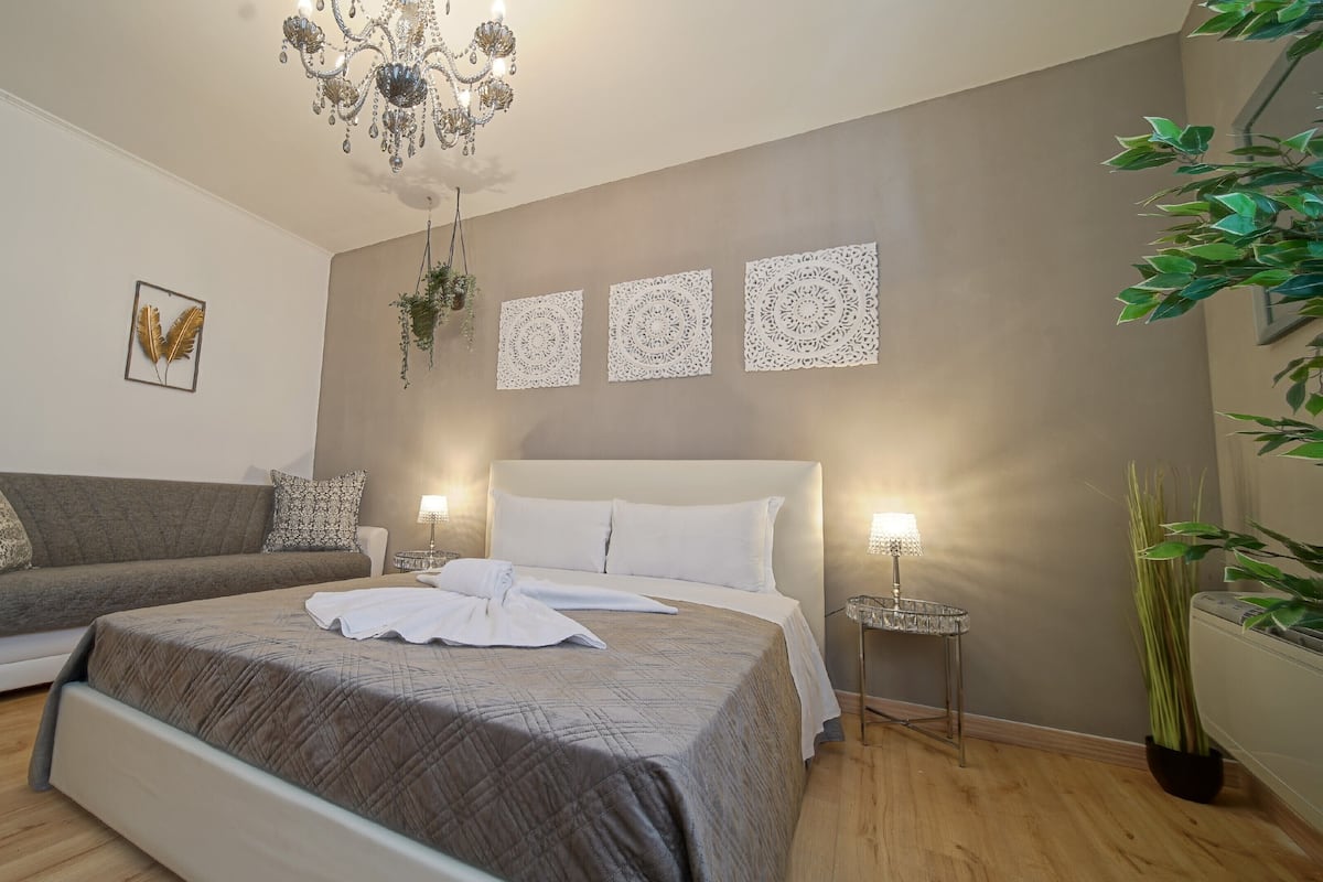 A bedroom with a bed, a sofa, a chandelier, and decorative wall art.
