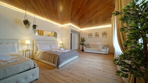 Une chambre d’hôtel avec un plafond en bois, deux lits, un canapé et plusieurs plantes en pot.
