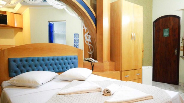 A neatly made bed with a blue headboard, a wooden wardrobe, and a door with a sign. - Hotel Mooca São Paulo (São Paulo)