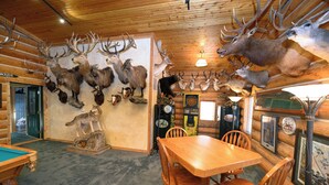 A wooden interior with a dining area, a pool table, and various mounted animal heads on the walls. - Secluded & Spacious Log Cabin Lodge Located in Western Nebraska - Pet-friendly! (Lodgepole)