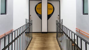 Ein Korridor mit zwei Türen, die mit 101 und 102 beschriftet sind, einem Holzboden und schwarzen Geländern mit orangenen Akzenten.
