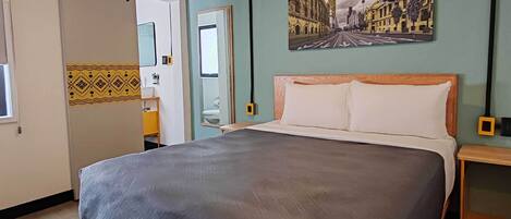 Une chambre à coucher avec un lit, un miroir, une porte et un tableau représentant un paysage urbain accroché au mur.