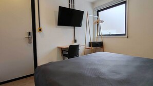 Ein Hotelzimmer mit Bett, Schreibtisch, Stuhl, einem an der Wand montierten Fernseher und einem Fenster mit Blick.