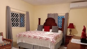 Un dormitorio con cama, una mesita de noche de madera, una lámpara roja y una ventana con reja de metal.