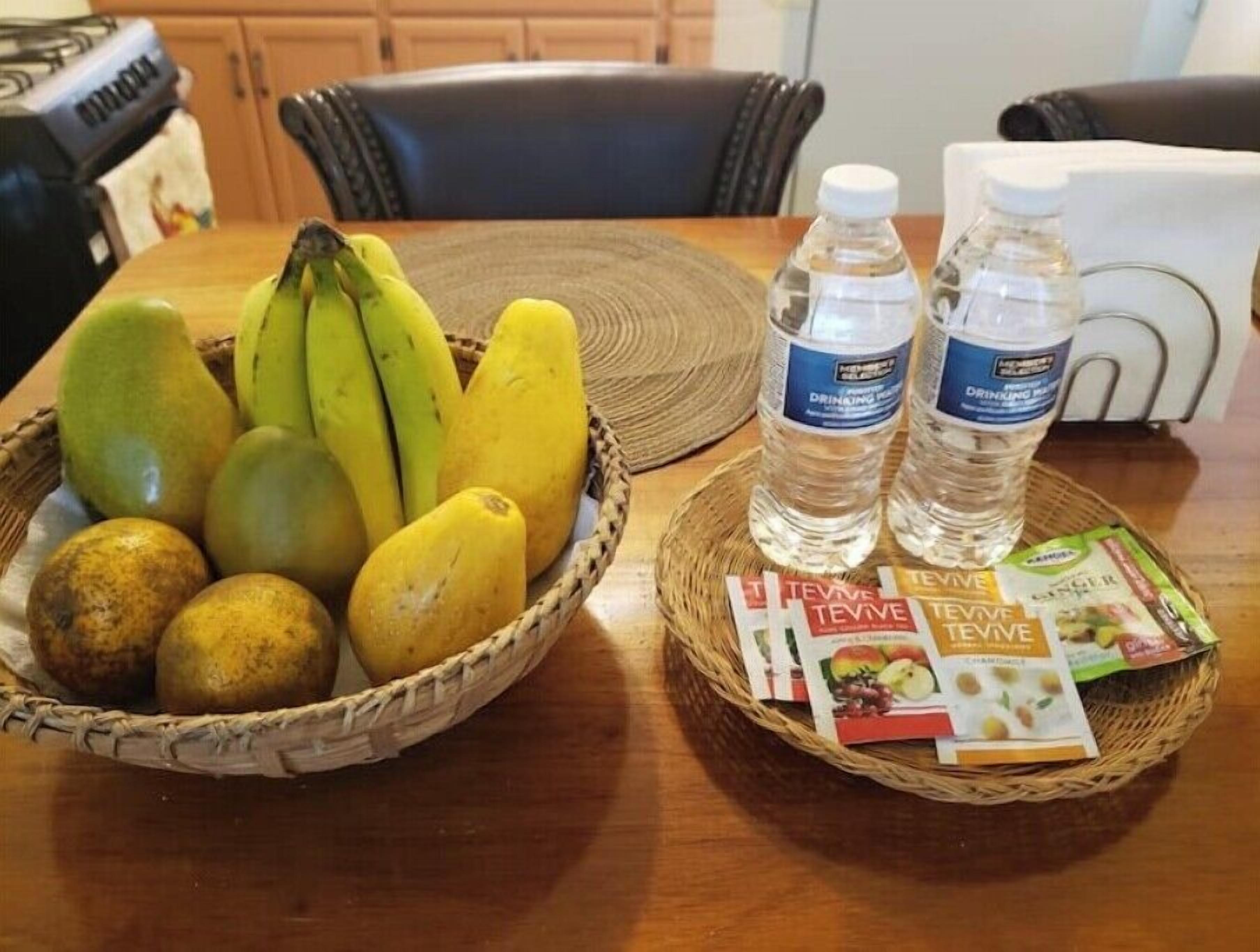 Une table à manger avec un panier de fruits, des bouteilles d’eau et un plateau de différents plats.