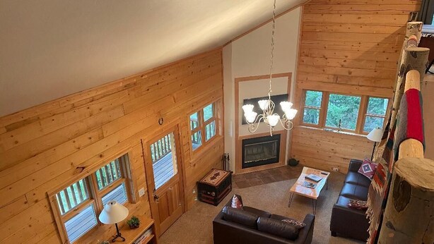 A cozy cabin interior with a fireplace, wooden walls, a sofa, and a staircase. - Mountain Meadow Cabin in Cotopaxi on 40 acres (Cotopaxi)