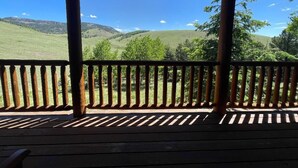 A wooden deck with a railing overlooking a grassy landscape with hills and trees. - Mountain Meadow Cabin in Cotopaxi on 40 acres (Cotopaxi)