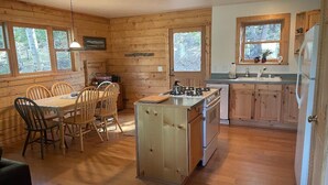 A cabin-style kitchen with wooden walls, a dining table with chairs, a stove, and a refrigerator. - Mountain Meadow Cabin in Cotopaxi on 40 acres (Cotopaxi)
