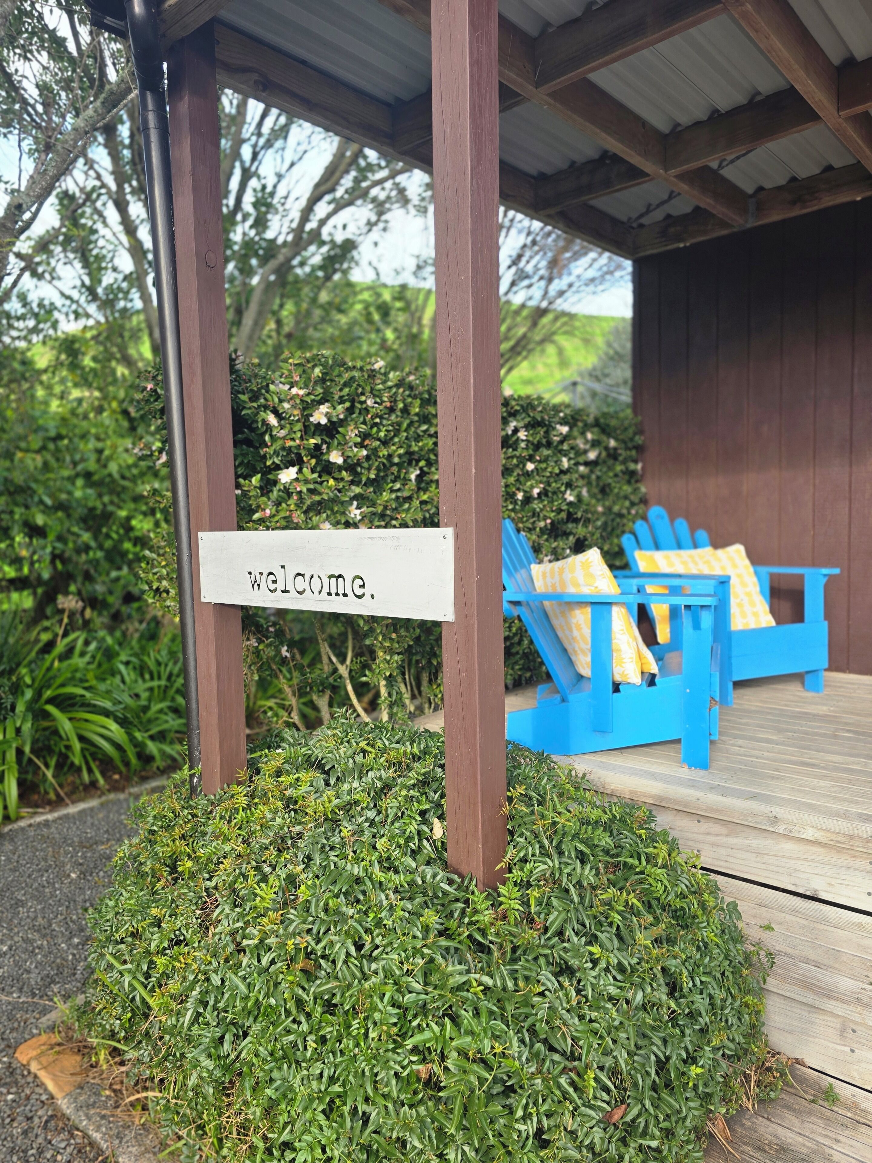 A wooden structure with a 'welcome' sign, blue chairs with yellow cushions, and a wooden deck.
