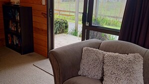 Una habitación acogedora con un sofá marrón, una estantería y un amplio ventanal con vistas a un paisaje verde.