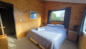 Un dormitorio con paneles de madera, una cama, una mesita de noche, una lámpara y una ventana con cortinas.