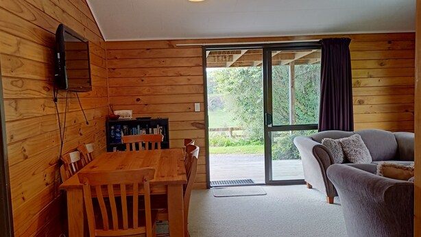 Un interior de madera con una mesa de comedor, sillas, un sofá y un televisor montado en la pared.