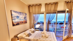 Un dormitorio con una cama grande, una mesita de noche con lámpara, un cuadro en la pared y vistas al exterior a través de una puerta corrediza de vidrio.