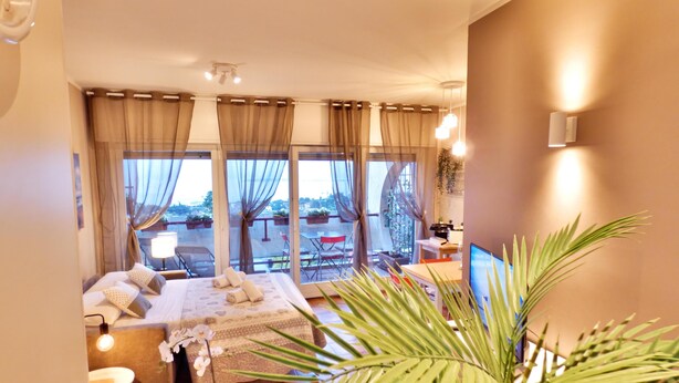 Un dormitorio moderno con cama, mesitas de noche, un escritorio y un ventanal con cortinas.