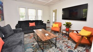 A living room with a dark grey sofa, orange armchairs, a wooden coffee table, and a large flat-screen TV. - "Good Vibes" 4 Wonderful Seasons @ Portland Home! (Portland)