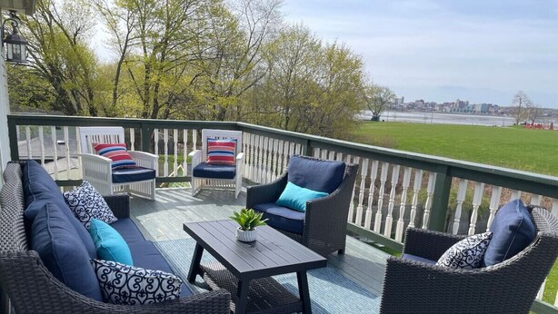 Een terras met rieten meubels, een tafel en uitzicht op een grasveld en gebouwen in de verte.