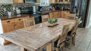 Een moderne keuken met houten kastjes, een grote houten eettafel en een roestvrijstalen koelkast.