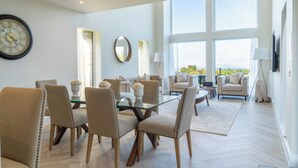 A spacious living area with a glass dining table surrounded by chairs, a large round clock, and a sofa. - Essich Park - 3BR - Hot Tub - Sleeps 6 (Essich)