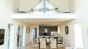 A spacious living area with a glass balustrade, a dining table with chairs, and a kitchen in the background. - Essich Park - 3BR - Hot Tub - Sleeps 6 (Essich)